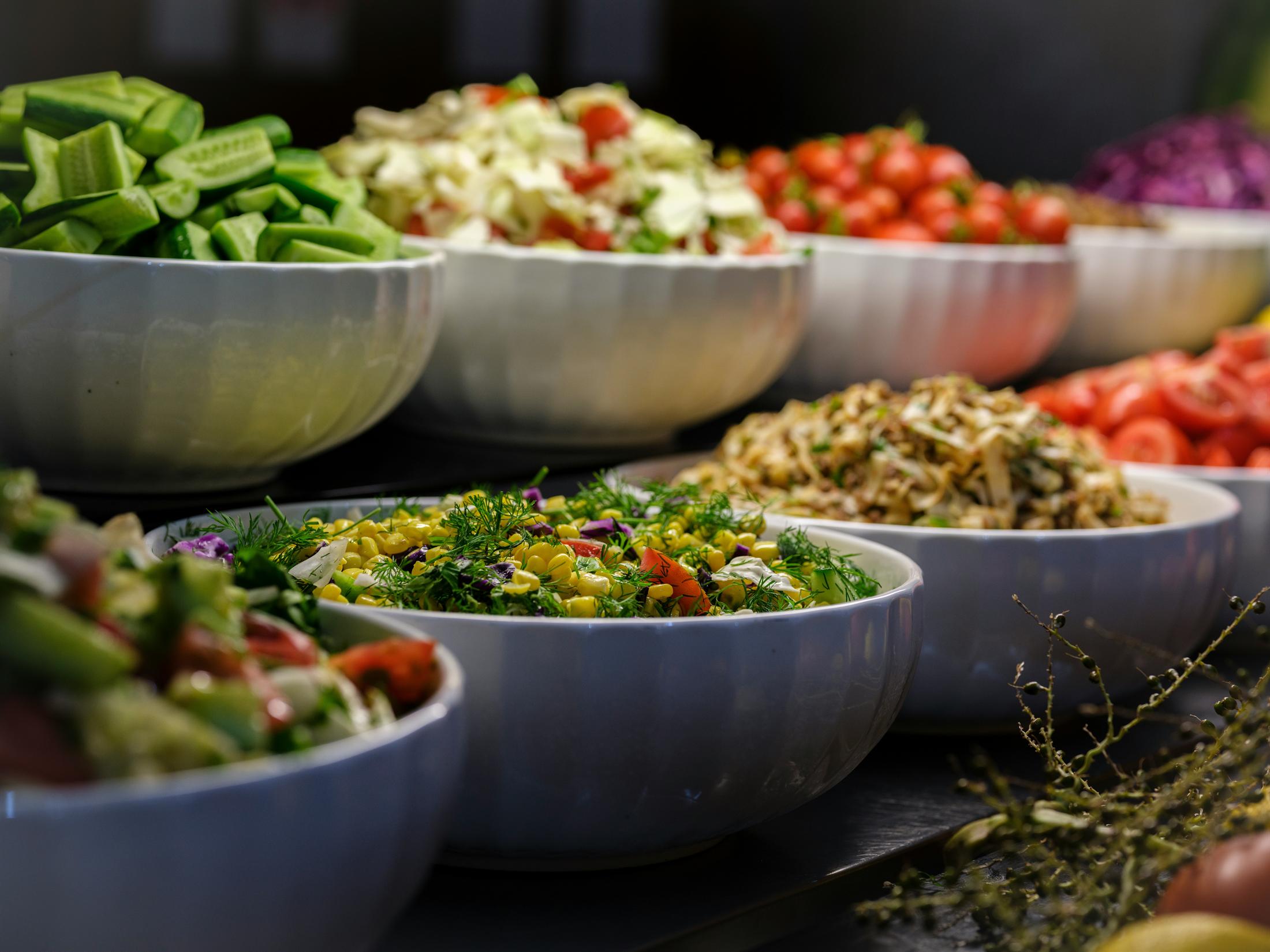 Fresh salads and prepared vegetables arranged for catered event service.